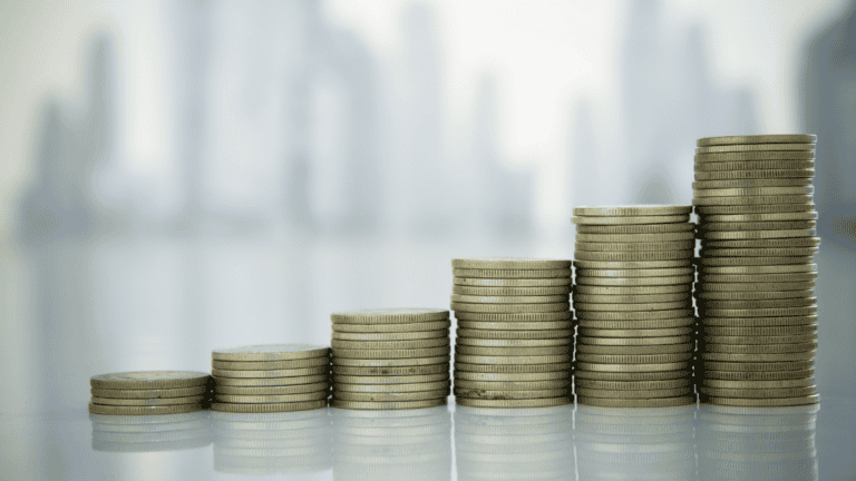 Stacked coins increasing in height against a blurred city skyline, representing steady law firm cash flow growth
