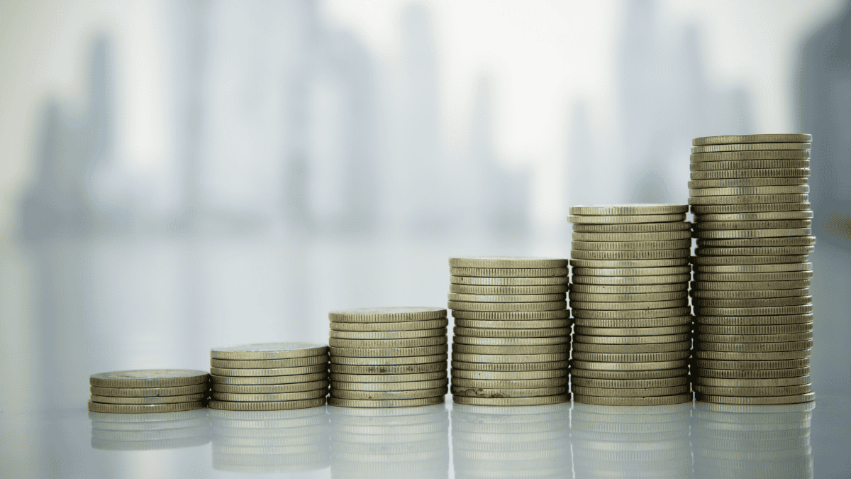 Stacked coins increasing in height against a blurred city skyline, representing steady law firm cash flow growth