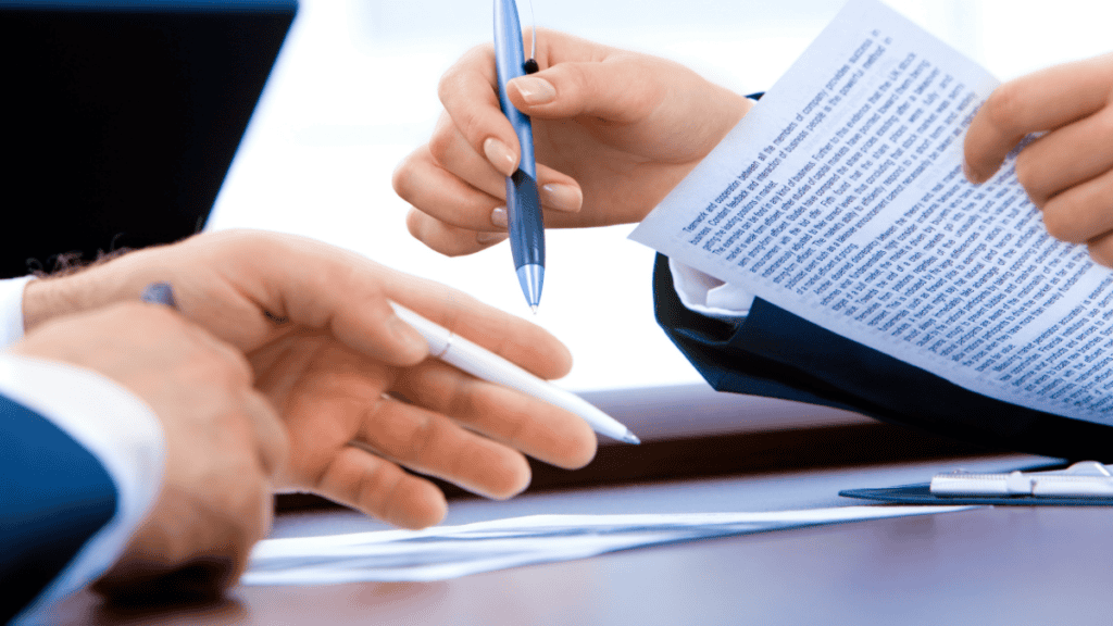 Two professionals exchanging pens while reviewing and signing off on financial documents, representing the sign-off step in the IOLTA reconciliation process
