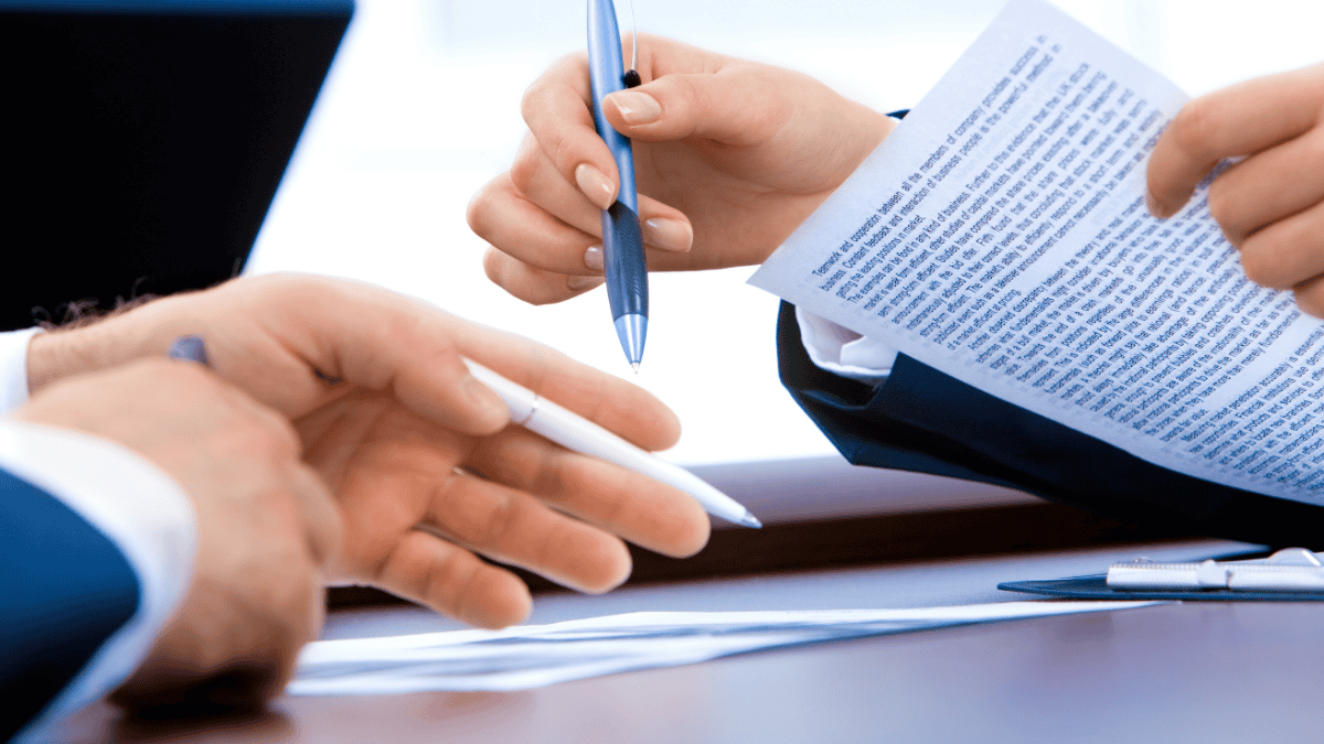 Two professionals exchanging pens while reviewing and signing off on financial documents, representing the sign-off step in the IOLTA reconciliation process