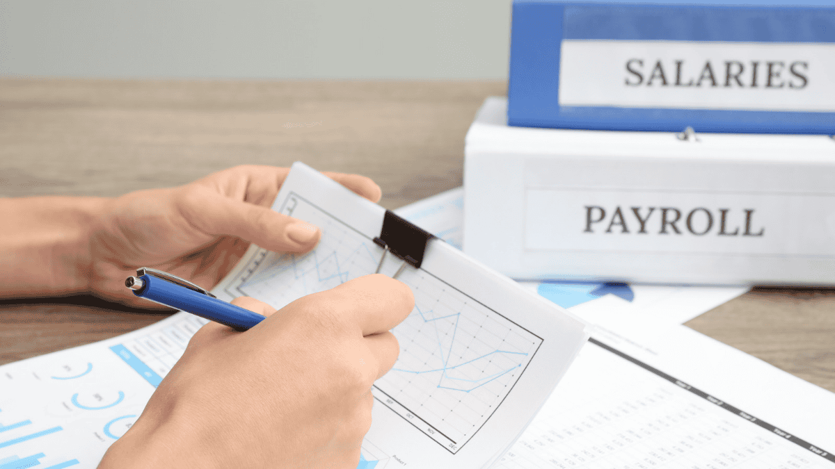Close-up of hands reviewing a salary trend chart with a pen, with Payroll and Salaries binders in the background, illustrating reasonable compensation for law firm owners
