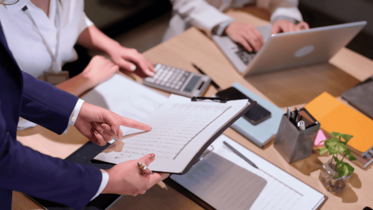 Advisor pointing to handwritten entries in a ledger while reviewing a law firm's financial statements with a calculator and laptop nearby